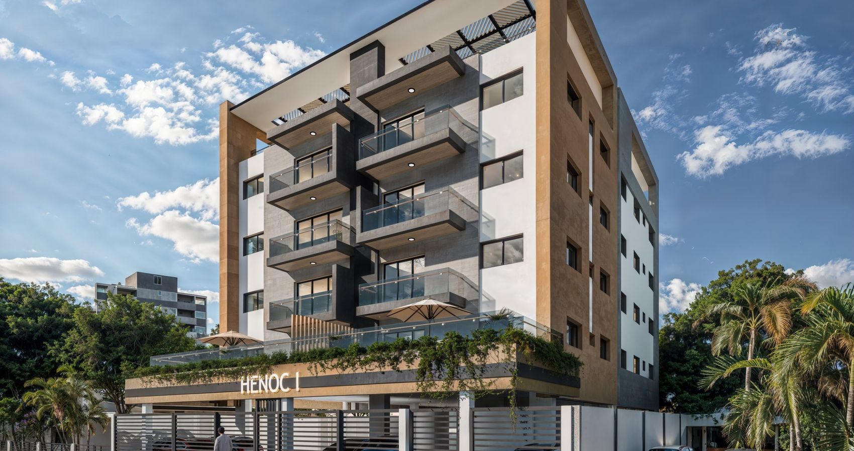 Render diurno de Residencial Henoc I visto desde la calle, con el letrero Henoc I en la entrada